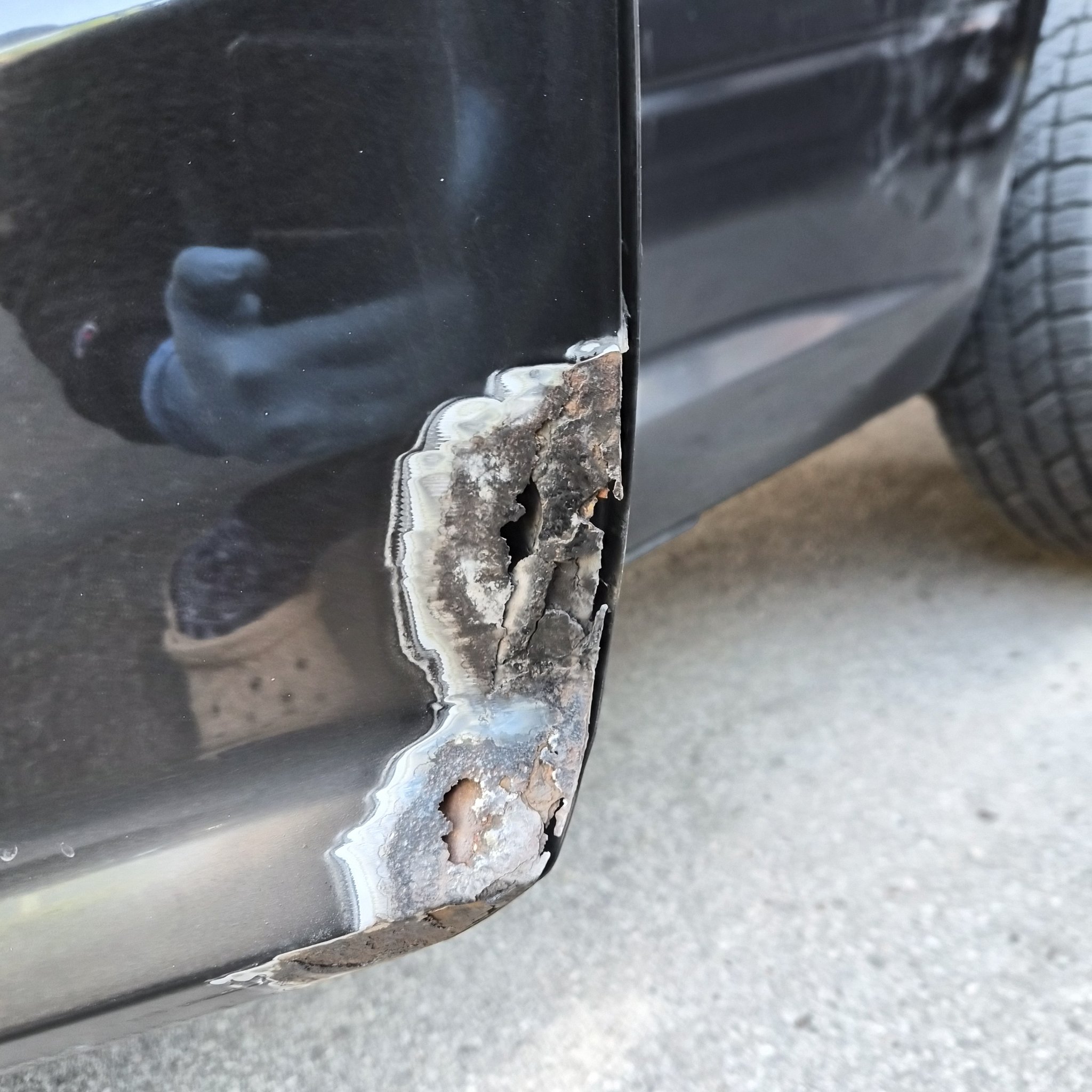 Rusted-through lower cab corner on the black Ram